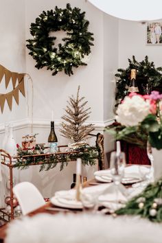 a dining room table set for christmas with wreaths on the wall and wine bottles