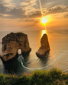 the sun is setting over two large rocks in the ocean with waves coming from them