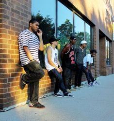 a group of young men standing in front of a brick building talking on their cell phones