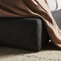 an unmade bed with a brown blanket on top of it and a black ottoman