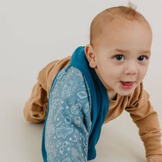 a baby crawls on one leg while wearing a blue bib and tan shirt