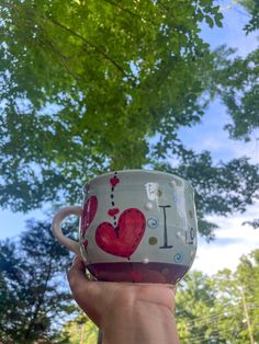 a hand holding a coffee cup with the word i love you on it in front of some trees