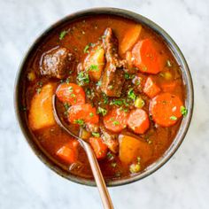 a bowl filled with stew and carrots on top of a white countertop next to a spoon