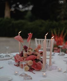 a table topped with lots of candles and flowers on top of a white table cloth