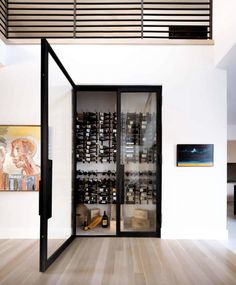 an open wine cellar in the middle of a room with wooden floors and black glass doors