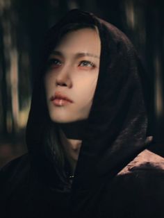 a woman with blue eyes wearing a black hoodie in the dark, looking into the distance