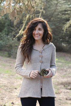 a woman is smiling while holding a pine cone in her hands and wearing a cardigan