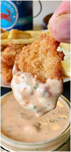 a person dipping some food into a small bowl with fries and dip sauce on the side