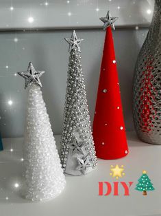 three christmas trees sitting on top of a white table next to a vase with silver stars