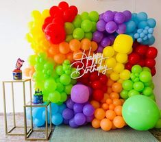 there is a rainbow colored balloon wall with happy birthday written on it