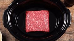 a square piece of raw meat in a black crock pot on a wooden table