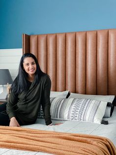 a woman sitting on top of a bed next to a brown headboard and pillows