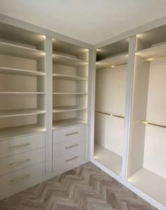 an empty walk in closet with white shelves and lights on the walls, along with chevron wood flooring