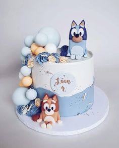 a blue and white cake with two cats on it's top, surrounded by balloons