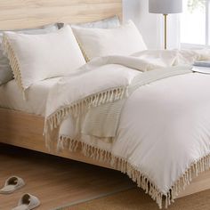 a bed with white linens and fringed edges on the headboard is shown