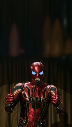 an iron man standing in front of a microphone and giving the thumbs up sign with both hands