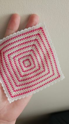 a hand is holding a crocheted square in white and pink yarn with a spiral design on it