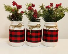 three mason jars decorated with pine branches and red berries