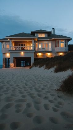 a large white house sitting on top of a sandy beach next to the ocean at night