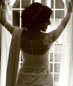 a woman standing in front of a window with her arms behind her head and wearing a white dress