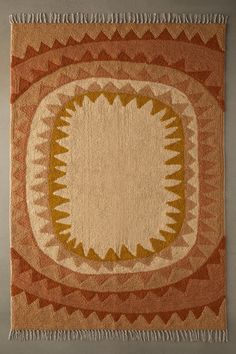 an orange and beige rug with fringes on the bottom is shown in front of a gray wall