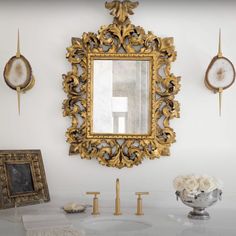 an ornate mirror hangs on the wall above a white vanity with gold faucets