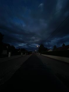 the dark street is empty at night with no one on it and there are clouds in the sky