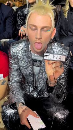 a man with his tongue out sitting in front of a group of people wearing metallic clothing