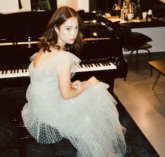 a woman sitting in front of a piano wearing a white dress with polka dots on it