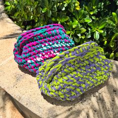 two colorful baskets sitting on top of a stone wall next to green bushes and shrubbery