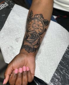 a woman's arm with a clock and rose tattoo on it, sitting on a chair