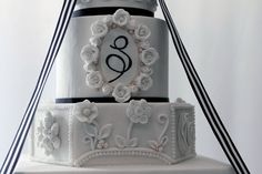 two tiered wedding cake with white flowers and black ribbon around the edges, decorated with monograms