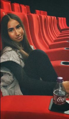 a woman sitting in a red chair next to a bottle of coke