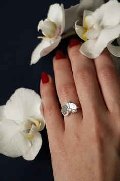 a close up of a person's hand with a ring on it and flowers in the background