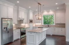 a kitchen with white cabinets and an island in the middle of the room is lit by two pendant lights