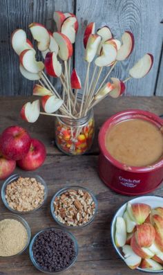 apples, cereals, nuts and chocolate in bowls on a wooden table next to an apple pot