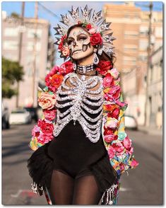 a woman with skeleton makeup and flowers on her head is standing in front of a street