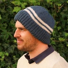 a man wearing a blue and white knitted hat with stripes on the side, standing in front of green leaves