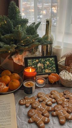 a table topped with cookies and oranges next to a christmas tree filled with candles