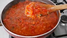 a wooden spoon in a pot filled with tomato sauce