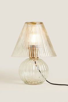 a glass table lamp with a gold base and pleated shade on the top, sitting on a white surface