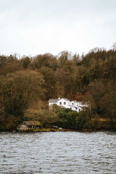 a white house sitting on top of a lush green hillside next to a body of water