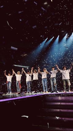 a group of young men standing on top of a stage holding hands in the air