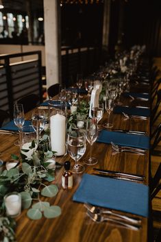 the table is set with wine glasses, candles and greenery