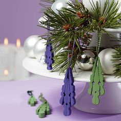 christmas decorations on a cake plate with candles in the background and pine branches hanging from it