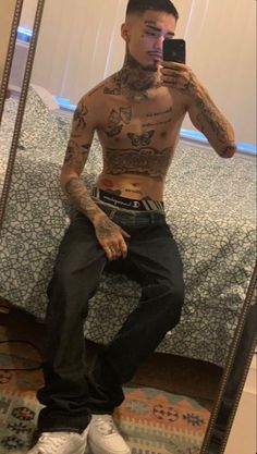 a tattooed man taking a selfie in front of a mirror with his cell phone