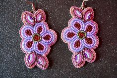 two purple and red beaded earrings sitting on top of a black table next to each other