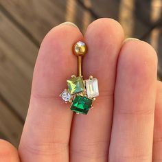 a person holding a green and white jeweled navel ring in their left hand