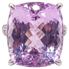 This stunning cocktail ring features an IGI Certified 24.20 Carat Kunzite in an intense purplish pink color and cushion shape, set in 18K white gold. The vibrant Kunzite gemstone is complemented by 30 white round brilliant diamonds totaling 0.47 carats, adding a touch of sparkle and elegance to the piece. The stylish design of the ring makes it perfect for daily wear, effortlessly combining luxury with versatility. The bold color of the Kunzite and the shimmer of the diamonds create a captivating and eye-catching piece that is sure to make a statement wherever it is worn. Luxury Kunzite Engagement Ring, Luxury Purple Kunzite Rings, Luxury Kunzite Ring For Formal Occasions, Cocktail Ring, Cocktail Rings, Round Brilliant, Bold Colors, Pink Color, Diamond Ring