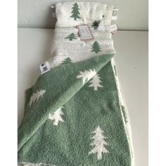 a green and white blanket with trees on it next to a tag hanging from the wall